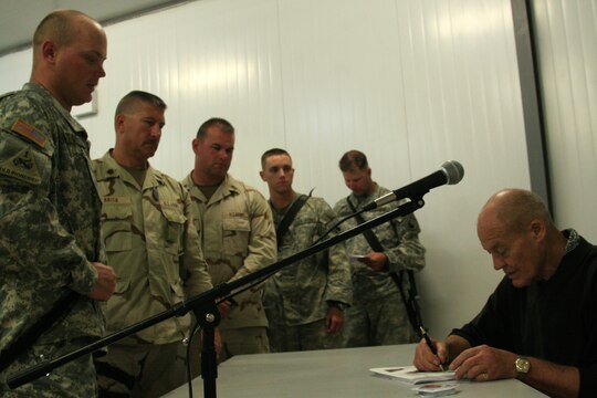 Retired Army Col. Robert L. Howard signs a copy of his citation of the Medal of Honor for a soldier at the Morale, Welfare and Recreation building at Al Asad, Iraq, April 20. Howard received the Medal of Honor March 12, 1968, for his gallant and intrepid actions in the Vietnam War. Leaving his helicopter landing zone and moving out to rescue a missing American soldier, his platoon came under attack by a two-company force. During the initial engagement, he was wounded and a grenade destroyed his weapon. Unable to walk, and seeing his platoon leader wounded, Howard crawled to his leader's aid. After dragging the seriously wounded officer back to the platoon area, Howard was able to rally the disorganized platoon and direct their fire upon the encircling enemy with shouts of encouragement. For three and a half hours, his small force repulsed enemy attacks enough to give rescue helicopters a chance to land. He personally supervised the loading of his men and would not leave the bullet-swept landing zone until all of his soldiers were aboard the helicopters safely.