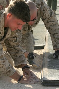 Lance Cpl. Kerry Boykin, (left), and Cpl. Jesse J. Marcellin pack dirt against the edge of the marshalling pad at Al Asad, Iraq, April 21, getting it ready for another piece to its jigsaw-like construction process. Both Marines are expeditionary airfield systems technicians with Marine Wing Support Squadron 274, Marine Wing Support Group 37 (Reinforced), 3rd Marine Aircraft Wing. Boykin is a native of Austin, Texas, and Marcellin is a Salt Lake City, native.