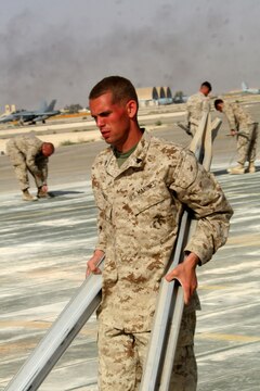 Cpl. Bryan Jones carries two stakes to the edge of the nearly completed marshalling pad at Al Asad, Iraq, April 21. Jones is an expeditionary airfield systems technician with Marine Wing Support Squadron 274, Marine Wing Support Group 37 (Reinforced), 3rd Marine Aircraft Wing. He is a Pittsfield, Mass., native.