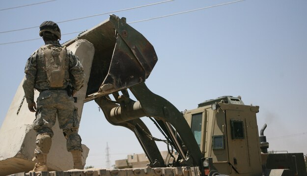 Marines and soldiers at Combat Outpost Falcon utilize an up-armored forklift, commonly referred to as a TRAM, to emplace over 300 concrete barriers June 26, 2006. The five Marines, a part of Combat Logistics Detachment 115, Combat Logistics Regiment 15, out of Camp Taqaddum, Iraq, aided the Army's 1st Brigade, 1st Armored Division in securing the combat outpost, a part of increased security operations in Southern Ramadi. (Official USMC photograph by Cpl. Daniel J. Redding. 060626-M-7799R-011. Released.)