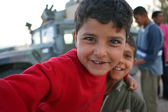 Local Iraqi children have fun while soldiers perform a vehicle search in a village near Camp Taqaddum, Iraq, March 12th, 2006. The soldiers from 2nd Battalion, 130th Infantry Regiment, performed a multi-faceted mission during a daylong operation as they carried out weapons cache sweeps, investigated possible improvised explosive devices and conducted route clearance operations. The Illinois-based National Guard took a few moments throughout the day to assist Iraqi villagers in the area, handing out supplies and spending time with the local children. The soldiers were grateful it wasnâ??t business as usual and could do something a little light hearted. Whether itâ??s handing out candy or searching for IEDs, the soldiers are proud of what they are doing in Iraq, said Sgt. 1st Class Timothy J. Atteberry, platoon sergeant. â??The individual, personal satisfaction of helping another human being really comes from these kinds of humanitarian-aid type missions,â? said Atteberry, a 38-year-old native of Champagne, Ill.::n::::n::The soldiersâ?? primary mission is to provide base security for the Marines and sailors of the forward-deployed 1st Marine Logistics Group. The 4,200 joint-service members of 1st MLG are part of the 25,000 Marines, airmen, solders and sailors of the 1st Marine Expeditionary Forceâ??s forward deployed element. The 1st MLGâ??s mission is to provide sustained logistics support to I MEF and Iraqi security forces operating in the Al Anbar province of Iraq. First MLG will also support the development of Iraqi Security Forceâ??s logistic capabilities in order to enable independent ISF led counter insurgency operations. ::n::