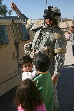 Although Spec. Shane B. Deaton, infantryman, cannot speak Arabic, he holds a conversation with local Iraqi children in a village near Camp Taqaddum, Iraq, March 12th, 2006. Deaton, 35, of Troy, Ill., and the other soldiers from 2nd Battalion, 130th Infantry Regiment, performed a multi-faceted mission during the daylong operation as they carried out weapons cache sweeps, investigated possible improvised explosive devices and conducted route clearance operations. The Illinois-based National Guard took a few moments throughout the day to assist Iraqi villagers in the area, handing out supplies and spending time with the local children. The soldiers were grateful it wasnâ??t business as usual and could do something a little light hearted. Whether itâ??s handing out candy or searching for IEDs, the soldiers are proud of what they are doing in Iraq, said Sgt. 1st Class Timothy J. Atteberry, platoon sergeant. â??The individual, personal satisfaction of helping another human being really comes from these kinds of humanitarian-aid type missions,â? said Atteberry, a 38-year-old native of Champagne, Ill.::n::::n::The soldiersâ?? primary mission is to provide base security for the Marines and sailors of the forward-deployed 1st Marine Logistics Group. The 4,200 joint-service members of 1st MLG are part of the 25,000 Marines, airmen, solders and sailors of the 1st Marine Expeditionary Forceâ??s forward deployed element. The 1st MLGâ??s mission is to provide sustained logistics support to I MEF and Iraqi security forces operating in the Al Anbar province of Iraq. First MLG will also support the development of the Iraqi Security Forces logistic capabilities in order to enable independent ISF led counter insurgency operations.