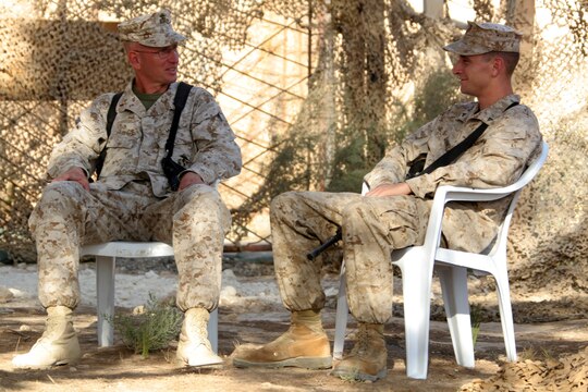 Chief Warrant Officer 3 Gary O. Quinney (left) and his son, Lance Cpl. Gary O. Quinney Jr., sit outside the father's office to catch up with each other before chow at Al Asad, Iraq, Sept. 13. Elder Quinney is the officer-in-charge of the Mortuary Affairs Collection Point Al Asad, Personnel Retrieval and Processing Detachment, Combat Logistics Battalion 7, 1st Marine Logistics Group (Forward). The younger Quinney is a tactical network specialist with communications platoon, Marine Wing Support Squadron 273, Marine Wing Support Group 37 (Reinforced), 3rd Marine Aircraft Wing (Forward). Both, father and son, haven't seen each other for more than two years until their paths crossed in Iraq. The father is a native of Mountain Home, Ark., and the son is a Beaufort, S.C., native.