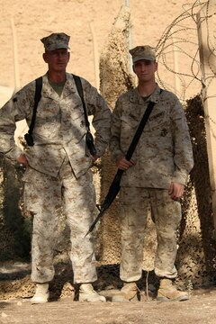 Chief Warrant Officer 3 Gary O. Quinney (left) and his son, Lance Cpl. Gary O. Quinney Jr., pose for a photo just outside the father's office at Al Asad, Iraq, Sept. 13. The elder Quinney is the officer-in-charge of the Mortuary Affairs Collection Point Al Asad, Personnel Retrieval and Processing Detachment, Combat Logistics Battalion 7, 1st Marine Logistics Group (Forward). The younger Quinney is a tactical network specialist with communications platoon, Marine Wing Support Squadron 273, Marine Wing Support Group 37 (Reinforced), 3rd Marine Aircraft Wing (Forward). Both, father and son, haven't seen each other for more than two years until their paths crossed in Iraq. The father is a native of Mountain Home, Ark., and the son is a Beaufort, S.C., native.
