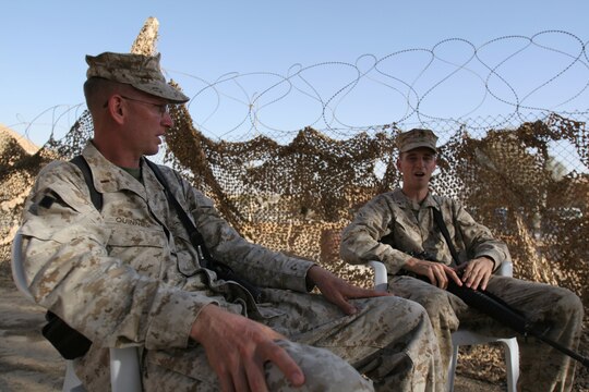Chief Warrant Officer 3 Gary O. Quinney (left) and his son, Lance Cpl. Gary O. Quinney Jr., sit outside the father's office to catch up with each other before chow at Al Asad, Iraq, Sept. 13. Elder Quinney is the officer-in-charge of the Mortuary Affairs Collection Point Al Asad, Personnel Retrieval and Processing Detachment, Combat Logistics Battalion 7, 1st Marine Logistics Group (Forward). The younger Quinney is a tactical network specialist with communications platoon, Marine Wing Support Squadron 273, Marine Wing Support Group 37 (Reinforced), 3rd Marine Aircraft Wing (Forward). Both, father and son, haven't seen each other for more than two years until their paths crossed in Iraq. The father is a native of Mountain Home, Ark., and the son is a Beaufort, S.C., native.