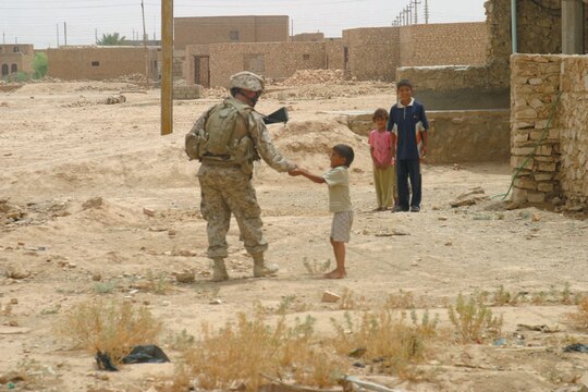 Corporal Jared W. Wagner, personal security detail, Jump Platoon, Headquarters and Service Company, 1st Battalion, 3rd Marine Regiment, hands a piece of candy to an Iraqi child during Operation Northwestern Shoulder.