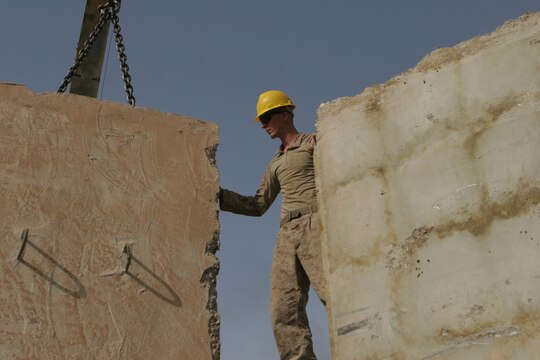 RAMADI, Iraq (August 21, 2008) – Lance Cpl. Steven T. Wise, a heavy equipment operator with Combat Logistics Company 111, Combat Logistics Battalion 1, 1st Marine Logistics Group helps guide a T-wall into place at the Ramadi Government Center on Aug. 21. The HE operators installed concrete walls throughout the compound to add additional protection for Coalition Forces and civilians who work there. “The T-walls we are installing today will block the view of buildings that surround the Government Center in the case of an enemy sniper,” said Cpl. Chris R. Yohe, HE operator with CLC-111. “The barriers hide the main walkways that are constantly being used within the center.” (Photo by Lance Cpl. Jacob A. Singsank)