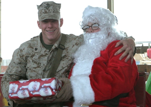 Cpl. Joshua A. Mendenhall, 23, Kansas City, Mo., motor transportation mechanic, Transportation Security Company, Combat Logistics Battalion 2, 1st Marine Logistics Group, receives a present from Santa Claus here Dec. 25. Two-hundred and fifteen Marines and Sailors each received a gift that was donated by family members and friends of the family of Capt. Tim P. Maloney, commanding officer, TS Co., CLB-2, 1st MLG. ?Being away from friends, family and home isn?t easy,? said Maloney, 30, Milton, Mass. ?To brighten up their Christmas, my wife Christina started coordinating and collecting donated gifts to send out here to the Marines and Sailors.? The platoon commanders of TS Co. collected a wish list from their troops to send back to the U.S. in November so the present would make it here by Christmas. ?Overall it shows that the people back home still truly care about the service members and what they do for our country.?