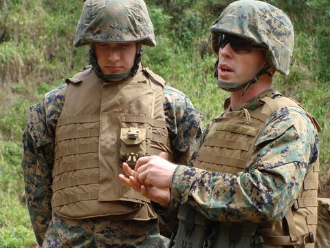 Sgt. Robert Manion (right), nuclear, biological and chemical NCO, demonstrates proper handling of the M67 hand grenade as Sgt. Shawn Davenport (left), Marine Air-Ground Task Force planner, attentively observes during a training exercise Feb. 25. MarForPac Marines spent the day learning about the M1014 shotgun and refamiliarization with hand grenades.