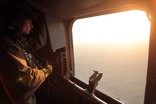 Cpl. Evan Shelton, a crew chief with the Marine Heavy Helicopter Squadron 361 (Reduced) (Reinforced) “Flying Tigers,” observes the immediate airspace as another CH-53E Super Stallion carries a disabled H-47 Chinook to Forward Operating Base Jalalabad, Afghanistan, for repairs Dec. 10.  An empty mount stands where a GAL-17 .50 caliber machine gun rests.  All additional cargo and weight was removed from both aircraft in preparation for lifting the 23,500 pound Chinook.