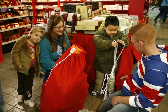 April Lombard and Devin N. Lynch, angel tree sponsors, gather around to watch the 5-year-old boy from the Yahata Children’s home open his gift at the 6th annual Marine Corps Exchange angel tree gift exchange Dec. 18th at the MCX.