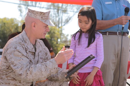 Col. Eugene N. Apicella presents Jae E. Yoon with the award for winning second place in the art/essay contest during the opening ceremony of the 17th annual Kids First Fair hosted by the Children, Youth and Teen Programs at the Paige Fieldhouse parking lot on Marine Corps Base Camp Pendleton April 28. "We are very appreciative of (Marine Corps Community Services) for allowing us to use the Kids First Fair for our presentation and recognition of the kids for their achievement," said George B. Brown, executive director of Armed Services YMCA for Camp Pendleton. Apicella is the deputy commander for Marine Corps Installations West, MCB Camp Pendleton. Yoon is a first grade student at Santa Margarita Elementary School.