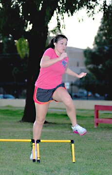 Maricela Tabarez, wife of Chief Petty Officer Matthew Tabarez, a SPAWAR employee, leaps over a hurdle as she completes a lap as part of Operation Throwdown. This is the second week of the class that Tabarez attends with more than 50 other participants.