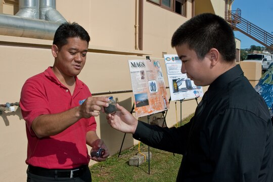 CAMP H. M. SMITH, HI - Donn Murakami, the U.S. Marine Corps Forces, Pacific Science Advisor, hands Damien Memorial High School junior chemistry student Brian Lab a small jar containing the waste residue produced by processing a large bag of garbage through the Micro Auto Gasification System (MAGS) Sept. 12.  The MAGS is a prototype being tested by MARFORPAC which reduces solid waste by as much as 95 percent while dramatically reducing carbon dioxide emissions.  The demonstration was part of the MARFORPAC Commander's Science, Technology, Engineering and Math (STEM) support program to local high schools. (USMC photo by Chuck Little)