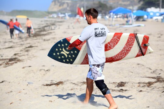 A surf camp participant makes his trek toward the ocean with an American Flag themed surfboard during a three-day surf camp at Camp Pendleton's San Onofre Beach, Aug. 12. Operation Amped held the sport therapy camp to provide surfing lessons to rehabilitating injured service members and their families.
