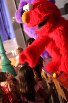 Elmo reaches down to shake hands and hug the children from on stage during the Sesame Street/USO Experience for Military Families show held at the Bulldog Box Office, Marine Corps Base Camp Pendleton, Aug. 14. This years show focuses on change and making new friends.