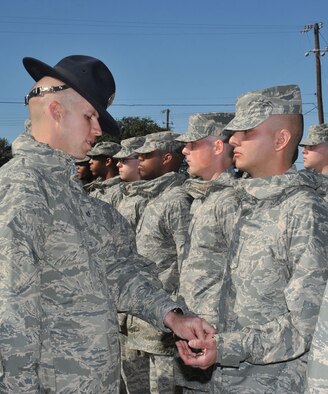Basic Military Training Instructor Staff Sgt. Eddie Glover, presents Airman Basic Justus Sanchez with the Airman’s Coin, symbolic of a service member's transition from trainee to Airman, during Thursday’s presentation at Joint Base San Antonio-Lackland. Sanchez's mother, Airman Basic Lori Huayacla, who is in week two of basic training, was able to attend her son's coining and graduation ceremonies. (U.S. Air Force photo/Alan Boedeker)