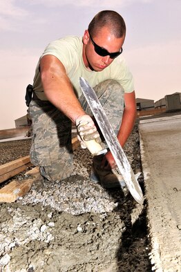 U.S. Air Force Airman 1st Class Jace McCarthy, 380th Expeditionary Civil Engineer Squadron pavement and construction equipment apprentice, deployed from Eielson Air Force Base, Alaska, removes excess concrete from a freshly paved pad at an undisclosed location in Southwest Asia. McCarthy is one of 20 "Dirt Boyz" responsible for constructing projects that will transition the base from expeditionary to enduring. (U.S. Air Force photo by Tech. Sgt. Christina M. Styer)
