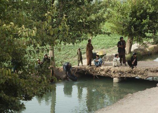 Local Afghans sit by a waterway and watch a convoy pass near Forward Operating Base Kajaki, Helmand province, Afghanistan, Aug. 4, 2013. A Marine Corps Community Services Marine with Combat Logistics Regiment 2, Regional Command (Southwest), visited the base to provide hard to find commodities to the isolated servicemembers. 