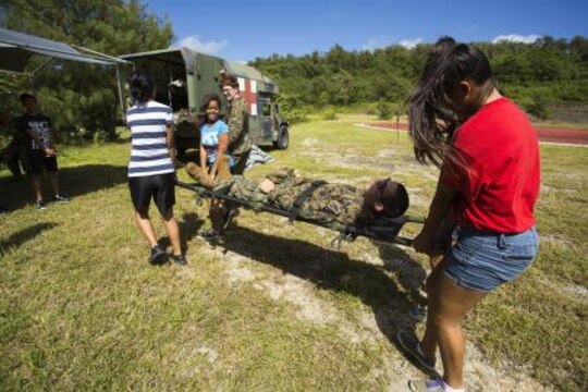 Petty Officer 3rd Class Sharon Fleer (standing center) from Lake Ozark, MO., uses Cpl. Nathan Evans from Sandy, OR., as a dummy to allow cadets the opportunity to understand how to use a stretcher during Combat Life Saver Course Nov. 22 at the Tinian Junior Senior High School Junior Reserve Officers’ Training Corps field. Cadets from TJSHS JROTC partook in a field meet with Marines and sailors to build camaraderie between one another. Fleer is a hospital corpsman and Evans is a data systems specialist. Both are with Marine Wing Support Squadron 171, Marine Aircraft Group 12, 1st Marine Aircraft Wing, III Marine Expeditionary Force.