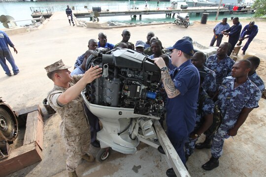 A group of sailors with the Togolese Navy watch as Lance Cpl. Tyler Jackson (left), a Marine with Special-Purpose Marine Air-Ground Task Force Africa 14.1, and Petty Officer 3rd Class Brian Spence, a Coastguardsman with U.S. Coast Guard Station Seattle, discuss small-boat engine mechanics in Lomé, Togo, March 25. Jackson and Spence put together a week-long training program of classroom instruction and practical application so the two groups of service members could partner together to fix engines. Established in 2011, Special-Purpose Marine Air-Ground Task Force Africa 14.1 is charged with supporting U.S. Africa Command and Marine Corps Forces Europe and Africa’s theater security cooperation requirements.
