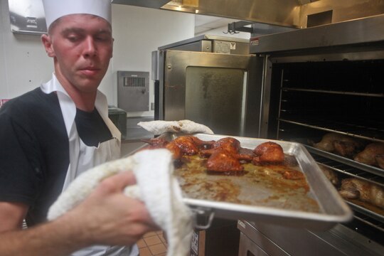 Corporal Clifton McReynolds, food service specialist, Headquarters Regiment, 1st Marine Logistics Group, handles a hot tray of chicken in preparation for lunch at the 14-area chow hall aboard Camp Pendleton, Calif., July 22, 2014. The 22-year-old was not excited to be a food service specialist at first, but he found a passion for working with people and now thrives in a job which enables him to serve and converse with hundreds of Marines daily.