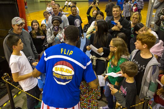 Service members and their families take photos with Harlem Globetrotters guard Saul ‘Flip’ White Dec. 9 at The Foster Field House on Camp Foster. The Harlem Globetrotters displayed their basketball artistry to service members and their families in a showdown with their rivals, the Washington Generals. The event was a part of the Harlem Globetrotters 13th military tour, in which the team travels overseas to U.S. military installations to provide memories of home during the holidays. The game was presented by Navy Entertainment, Leatherneck Tour and Marine Corps Community Services. 