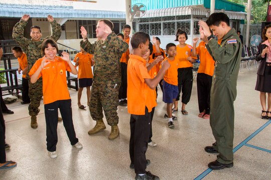 From left, Petty Officer 1st Class Amaflor Pinera, Petty Officer 3rd Class Joel Reidell and Flight Lt. Rungroj Pomwatthanamongkol dance with students from Nakhon Ratchasima Punyanukul School in Nakhon Ratchasima, Kingdom of Thailand, during a community relations event for exercise Cobra Gold 2014 Feb. 11. CG 14 is a joint, multinational exercise conducted annually in the Kingdom of Thailand aimed at enhancing and increasing multinational interoperability. Pomwatthanamongkol is a pilot with Squadron 401, Wing 4, Royal Thai Air Force. Pinera is an x-ray technician with Marine Wing Support Squadron 171, Marine Aircraft Group 12, 1st Marine Aircraft Wing, III Marine Expeditionary Force. Reidell is a field medical technician from MWSS-171.