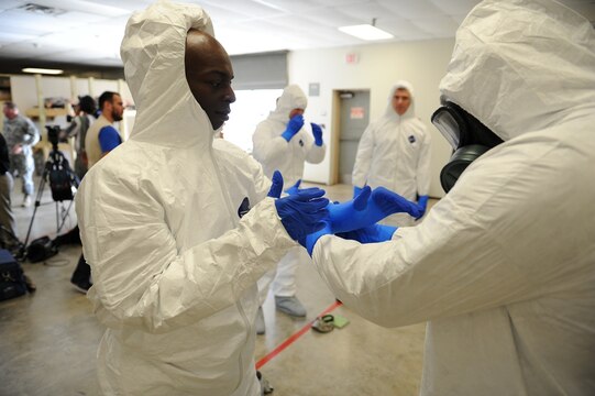 Sgt. 1st Class Venrick James (right), a 36th Engineer Brigade Soldier, helps Maj. John Dills, the 36th Engineer Brigade chief of current operations, put on his nitrile gloves during training inside the Medical Skills Training Center at Fort Hood, Texas, on Oct. 9. Scott Paris, a Marine Corps Systems Command civilian and joint program manager for protection, is working to improve personal protective equipment like this to better protect aid workers in the fight against the Ebola outbreak in West Africa.