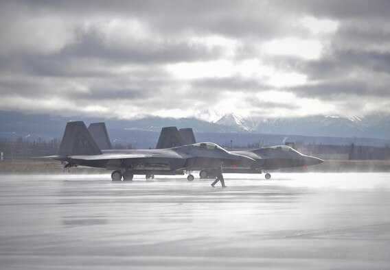 A crew chief walks past two F-22 Raptors parked on Joint Base Elmendorf-Richardson, Alaska, April 8, 2015. After a weather hold, the Airmen made it possible for pilots of the 90th Fighter Squadron to execute a training mission where they penetrated simulated enemy airspace, and dropped Joint Direct Attack Munition guided bombs on a target area adjacent to Eielson Air Force Base, Alaska. (U.S. Air Force photo/Justin Connaher)