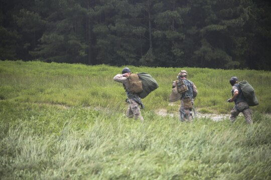 Marine jump masters and a sailor with 2nd Radio Battalion make their way across Landing Zone Canary following flight operations aboard Marine Corps Base Camp Lejeune, N.C., Aug. 18, 2015. Cargo and Marines were air-dropped from an MV-22 Osprey at varying altitudes. (U.S. Marine Corps photo by Cpl. Paul S. Martinez/Released)