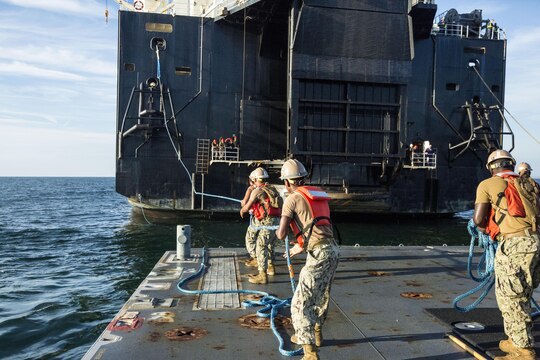 Sailors with Naval Beach Group 2 pull a rope in from the USNS 1st Lt. Jack Lummus to attach to a Roll-on/Roll-off Discharge Facility, during a Marine Prepositioning Force Exercise, Aug. 19, 2015. Marines with Combat Logistics Regiment 25 and sailors with NBG-2 joined forces for the latest iteration of MPFEX, which saw service members offloading the Lummus using Lift-on/Lift-Off and Roll-on/Roll-off procedures off the coat of Marine Corps Support Facility Blount Island, Fla. (U.S. Marine Corps photo by Sgt. Shawn Valosin/Released)