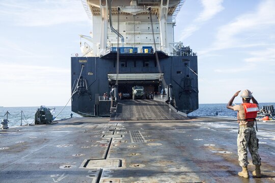 A sailor with Naval Beach Group 2 directs a seven-ton truck off of the USNS 1st Lt. Jack Lummus and onto a Roll-on/Roll-off Discharge Facility (RRDF), during an in-stream Marine Prepositioning Force Exercise, Aug. 19, 2015. Marines with Combat Logistics Regiment 25 and sailors with NBG-2 joined forces for the latest iteration of MPFEX, which saw service members offloading the Lummus using Lift-on/Lift-Off and Roll-on/Roll-off procedures off the coast of Marine Corps Support Facility Blount Island, Fla. (U.S. Marine Corps photo by Sgt. Shawn Valosin/Released)