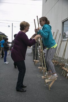 Paula Smedes, a program assistant with the Youth and Teen Center at Marine Corps Air Station Iwakuni, Japan, helps her daughter, Rhianna Smedes, walk on bamboo stilts during Cultural Day in Tsuzu, Dec. 12, 2015. During this cultural exchange visitors participated in a variety of activities such as mochi pounding, making wooden flutes, and walking on bamboo stilts, building friendships between the people of both cultures.