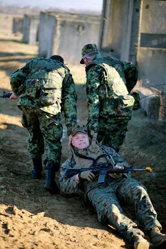 Lance Cpl. Michael Taylor grins for the camera as he plays the part of a casualty being dragged to safety by Cpl. Trivunovic Milan (left) and Master Sgt. Ivan Tucic (right). Serbians conducted MOUT training with Marines at Novo Selo training area in Bulgaria, Jan. 17, 2015 as part of Exercise Platinum Lion.