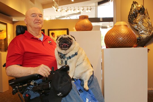 Jim Russell sits in the middle of the The Janice Griffiths Gallery with his rotund service pug, Mr. Beau, resting on his lap. The dim lights and cool interior of the gallery offer both some relief from the heat of the day as Russell recounts his tale of his life journey from military discipline to artistic expression.  