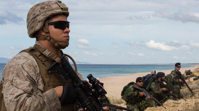 A U.S. Marine with the 26th Marine Expeditionary Unit, from the USS Arlington (LPD-24) holds security with Portuguese Marines at Pinheiro Da Cruz, Praia Da Raposa beach in Portugal, while participating in a combined amphibious assault exercise, Oct. 20, 2015, during Trident Juncture 15. Trident Juncture is a NATO-led exercise designed to certify NATO response forces and develop interoperability among participating NATO and partner nations.