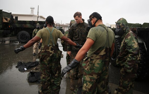 Lance Cpl. William Hony, center, chemical, biological, radiological and nuclear chief with Marine Wing Support Squadron 171, inspects reconnaissance, surveillance and decontamination Marines mission-oriented protective postures four gear during a simulated chemical attack at the MWSS-171 motor transportation wash rack at Marine Corps Air Station Iwakuni, Japan, Nov. 18, 2015. As part of an operational decontamination exercise, the RSD team decontaminated vehicles, and performed a MOPP exchange to thoroughly review each other’s PPE and ensure Marines could safely resume normal operations.