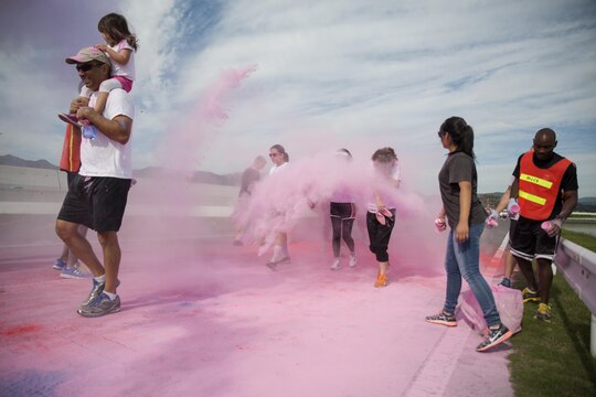 Volunteers throw colored powder at participants running by during the Color Me Awareness Run at Penny Lake Field at Marine Corps Air Station Iwakuni, Japan, Oct. 3, 2015. Behavioral Health and Health Promotions coordinated this event to raise the awareness of substance abuse, domestic violence and breast cancer.
