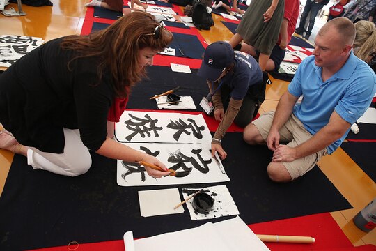 Gunnery Sgt. Victor Mancini, maintenance control staff non-commissioned officer with Marine Aerial Refueler Transport Squadron 152, aboard Marine Corps Air Station Iwakuni, Japan (right), and his wife, Arlene Mancini (left), compete against Japanese locals in a calligraphy contest during a cultural adaption program trip to the annual Japanese Calligraphy Brush Festival, in Kumano, Hiroshima Prefecture, Sept. 23, 2015. This cultural trip is one of many events coordinated to assist service members and their families adapt to the Japanese lifestyle. 