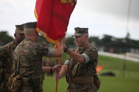 Col. Sean M. McBride, right, passes the III MEF Headquarters Group colors to Col. Brian M. Howlett, left, June 9 at Parade deck on Camp Hansen.