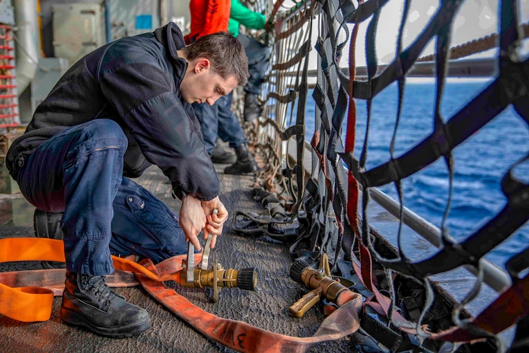 A sailor tightens a nozzle on a fire hose.