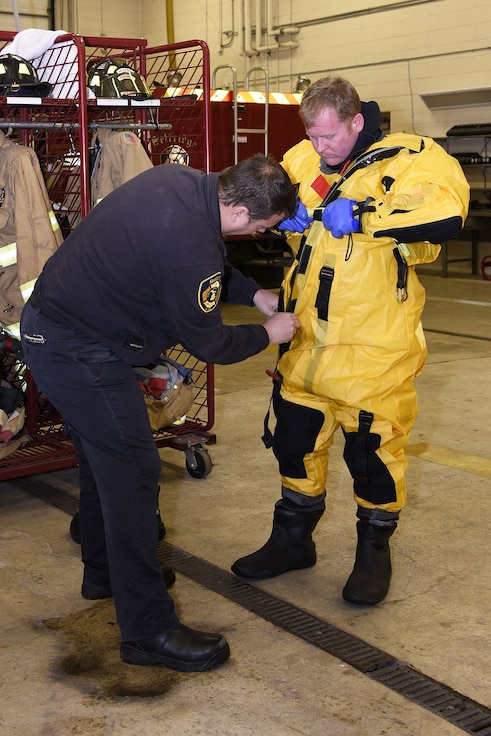 Gary Stringer helps Ed Hirth, both firefighters with the 127th Civil Engineer Squadron, assigned to the Selfridge Air National Guard Base fire department, don a cold-water emergent suit to prepare for an ice rescue training exercise on Lake St. Clair, Harrison Township, Mich. on Jan. 31, 2017.