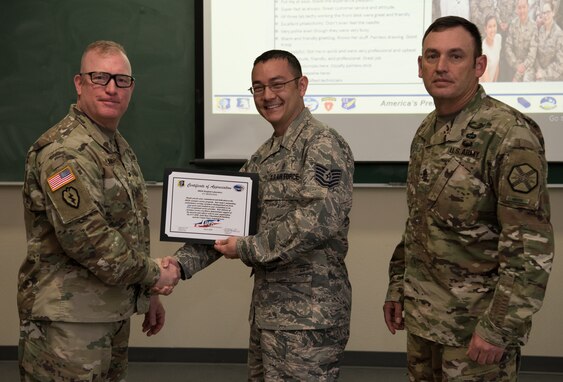 U.S. Army Col. Adam Lange, 673d Air Base Wing and Joint Base Elmendorf-Richardson vice-commander, and U.S. Army Sgt. Maj. Jerry Byrd, Garrison Sgt. Maj. for 673d Air Base Wing, present a certificate of recognition to a member of the JBER Hospital Laboratory, at JBER, Alaska, June 15, 2018. The certificate recognizes the team for exceptional customer service.