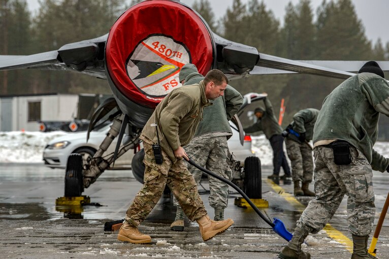 Airmen shovel and sweep slush and ice away from F-16 Fighting Falcons.