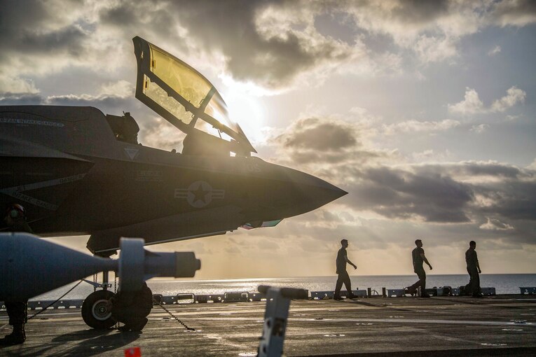 Marines walk on a flight deck near a large aircraft.
