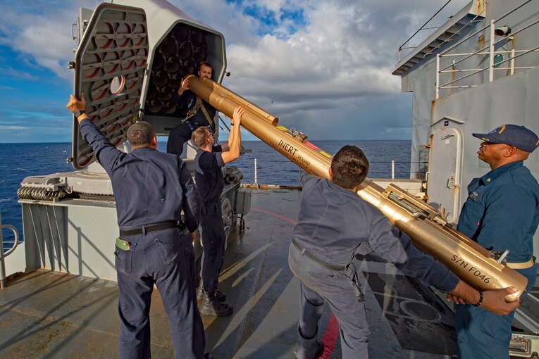 Five sailors load a training missile while on the deck of a ship.