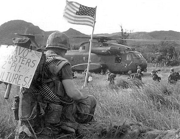 A Marine from 2nd Platoon "Vultures," of Bravo Company "Bushmasters," bares the Stars and Stripes while others from his unit board a CH-53A Sea Stallion with Marine Heavy Helicopter Squadron 463 in Vietnam in 1967. Initially a World War II bomber squadron, HMH-463, Marine Aircraft Group 16 (Reinforced), 3rd Marine Aircraft Wing, flew the first CH-53s in Vietnam with the main mission of providing assault support transport, which they still do today.