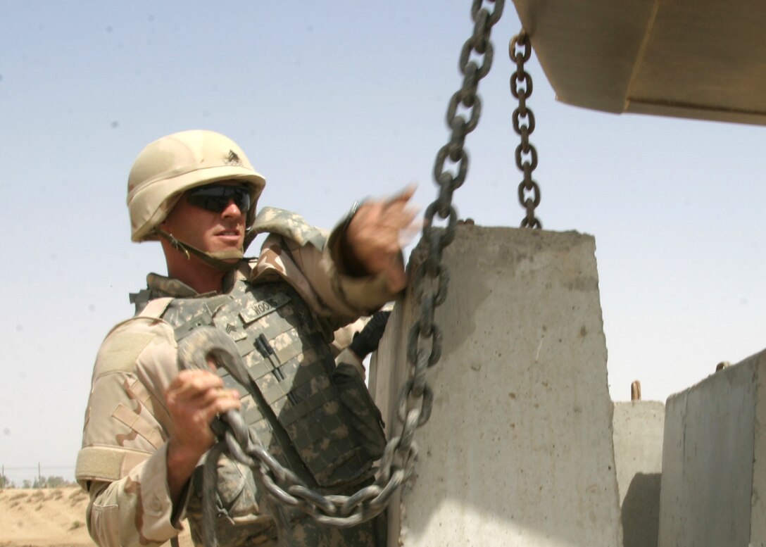 A soldier attaches a chain from a Texas barrier to a Five-yard loader at Camp Ramadi on May 12. The loader operator delicately places barriers into position along a newly constructed entrance road in Iraq.