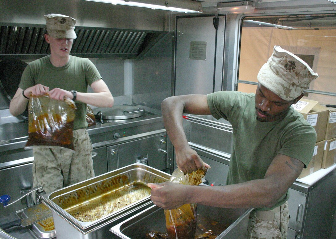 Corporal Sharod L. Wade, of Washington, D.C., tears open a freshly boiled bag of ribs while Lance Cpl. Kyle D. Fitzwater, of Chattanooga, Tenn., waits with another in a Field Food Service System aboard Forward Operating Base Hit, Iraq, Dec. 23, 2005.  Wade and Fitzwater are food service specialists assigned to the 2nd Marine Logistics Group who are currently supporting the 22nd Marine Expeditionary Unit (Special Operations Capable) as the unit conducts counterinsurgency operations in Iraq's Al Anbar province.